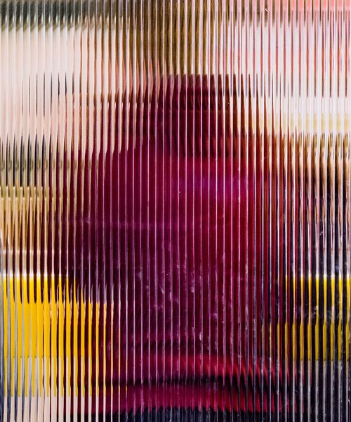 Unscharfe Silhouette hinter geriffeltem Glas mit rötlichen und gelben Farbtönen.